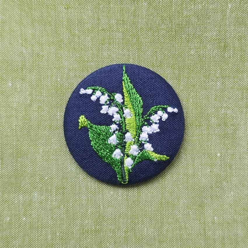 Petite broche brodée deux brins de muguet sur fond bleu marine porte-bonheur chance